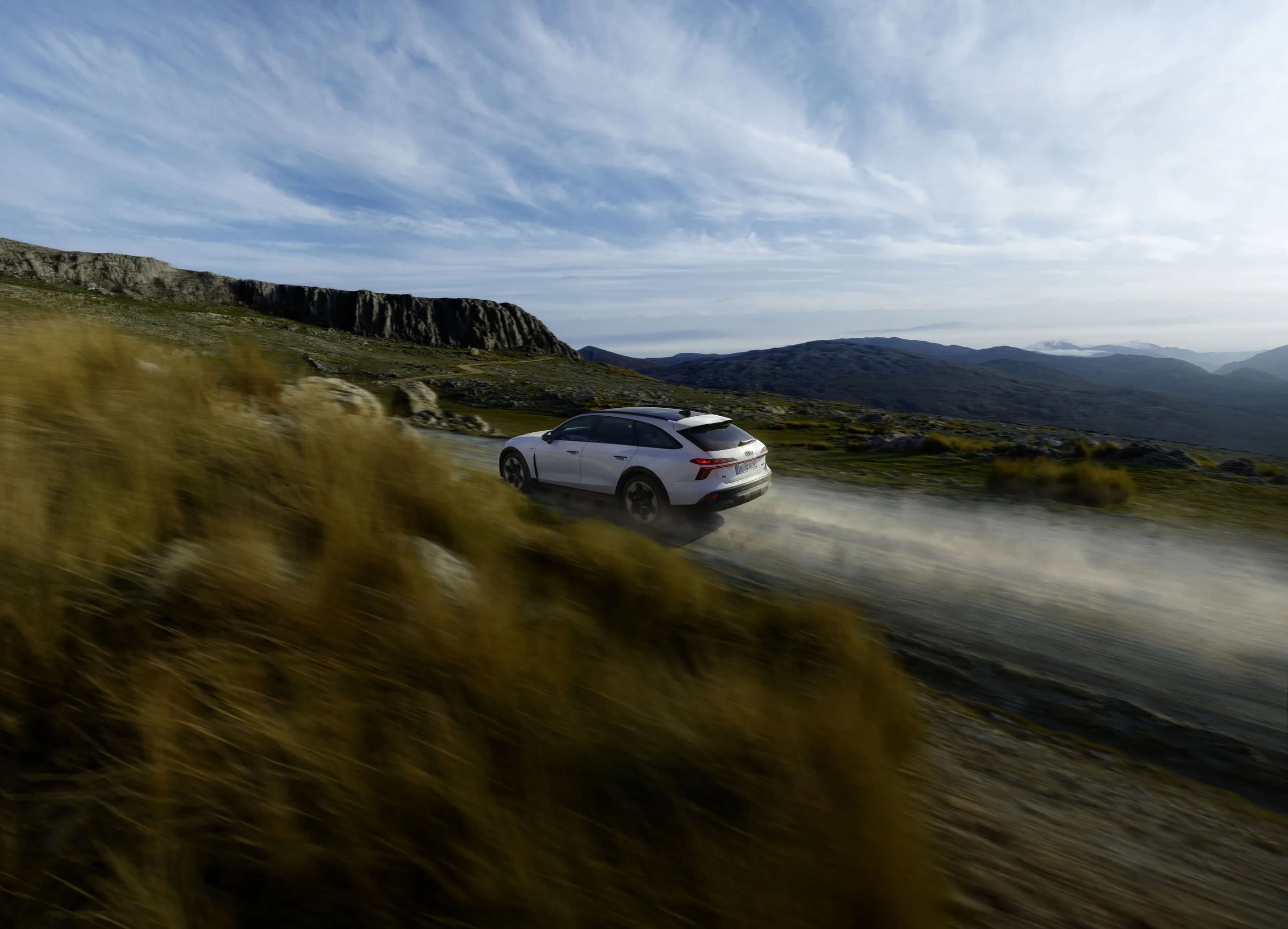 Audi A6 allroad e-hybrid - Dynamic shot: Audi A6 allroad e-hybrid (glacier white) on a gravel road in a mountainous landscape – dynamic and controlled beyond paved roads.
