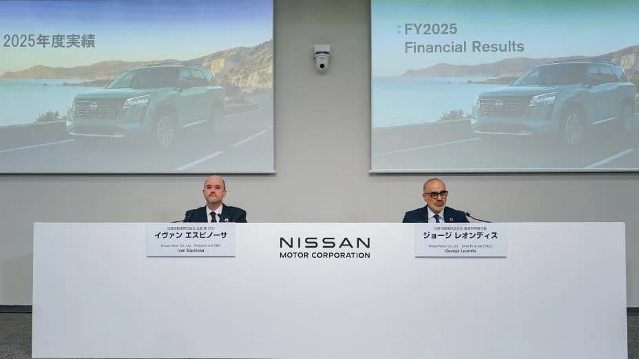 A press conference scene with two people seated side by side at the front of a conference room. Behind them, screens display images of vehicles and the text “FY2025 Financial Results,” with the “NISSAN MOTOR CORPORATION” logo shown on the central wall.