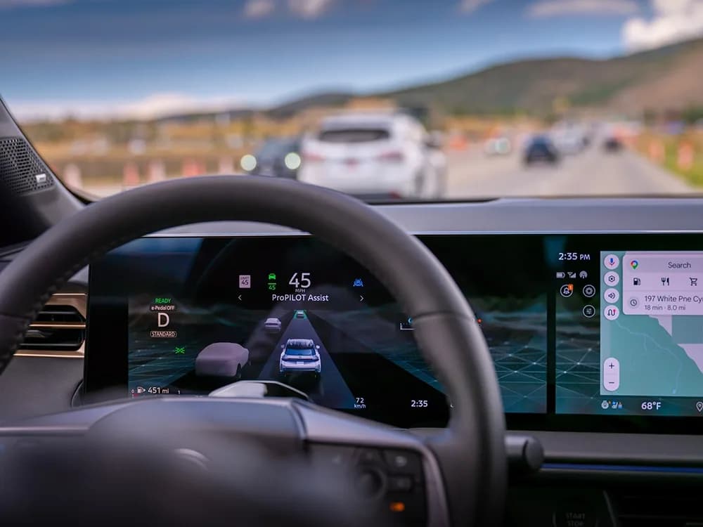 The dashboard vehicle display as seen through the steering wheel of the 2027 Nissan Rogue Hybrid SR.
