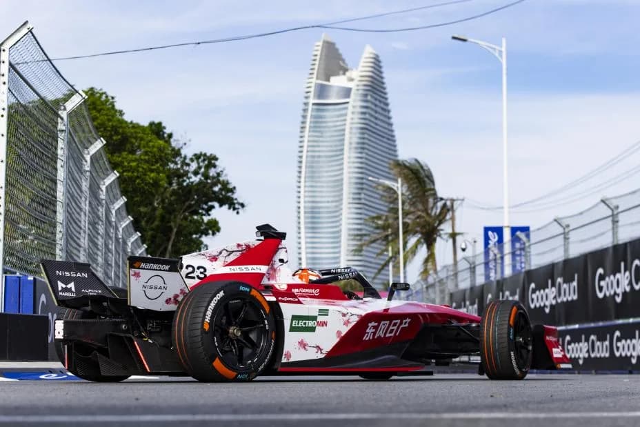 Rear/side shot of Norman Nato in the #23 Nissan e‑4ORCE 05 on-track in Sanya, with a skyscraper visible in the background of the image as well as trees either side of the circuit.