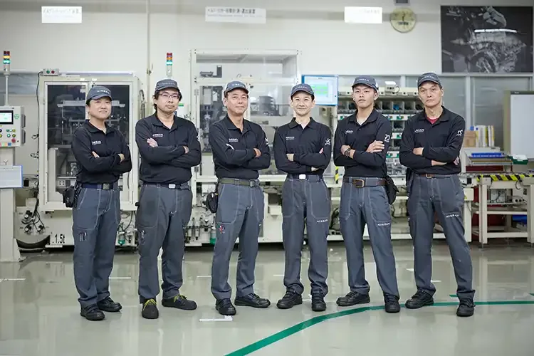 Six Nissan employees standing together in dark uniforms with their arms crossed.