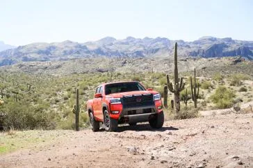 Front right 3/4 angle of the 2026 Nissan Frontier PRO-4X driving on arid landscape during the daytime.