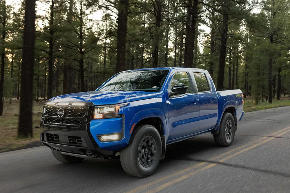 Front left 3/4 view of the 2027 Nissan Frontier Sport Edition driving along a tree-lined road.