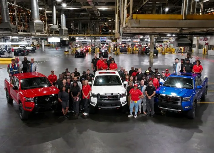 Three Nissan trucks parked on a warehouse floor with employees standing nearby for a picture.