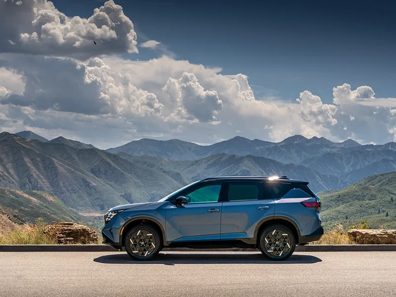 Left profile view of the 2027 Nissan Rogue Hybrid SR, mountains and clouds are behind.