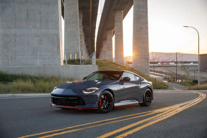 Front left 3/4 view of the 2027 Nissan Z NISMO MT curving under a highway bridge at sunset.
